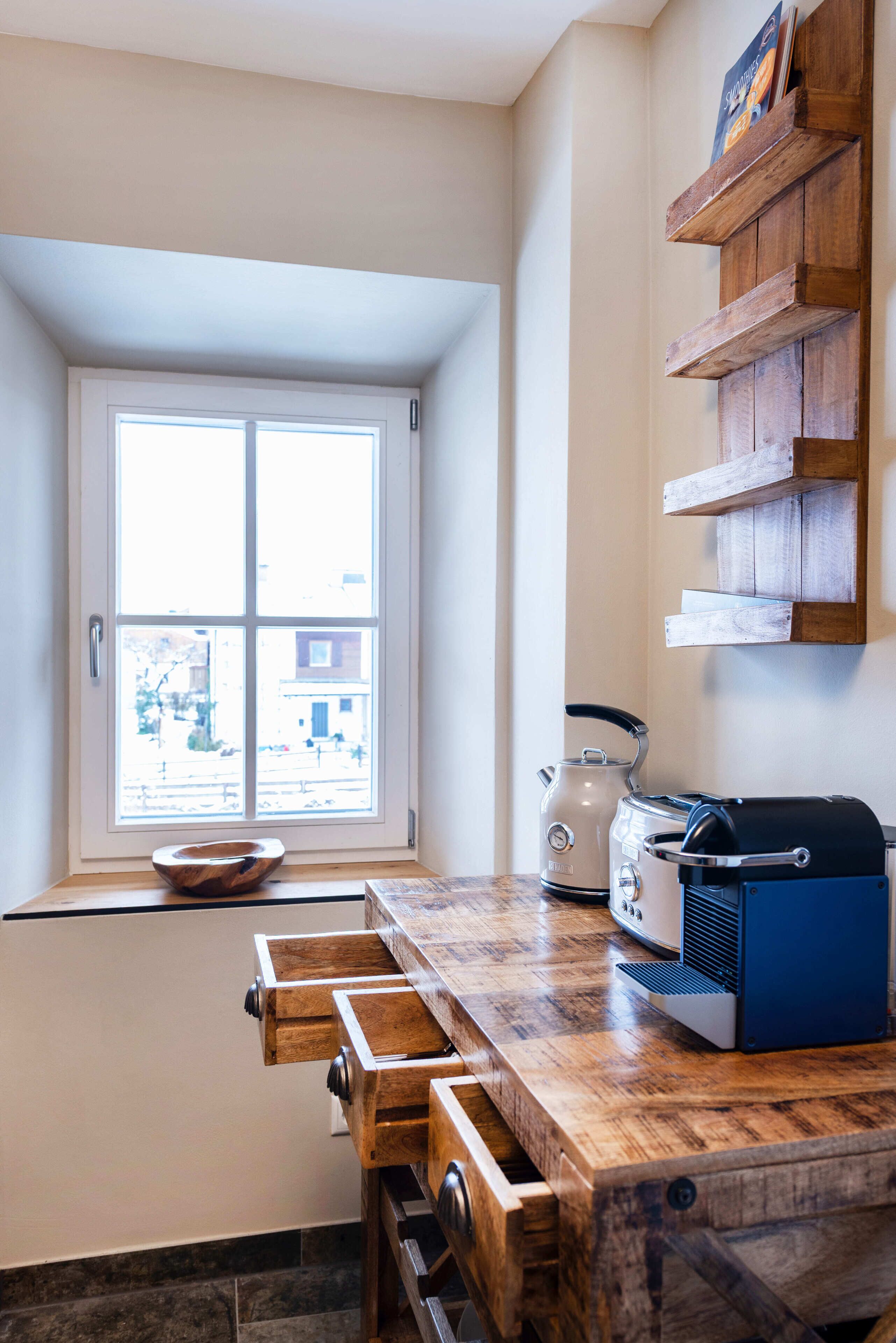 A kitchen with a wooden countertop, a kettle, a toaster, and a window with a view of the outside.