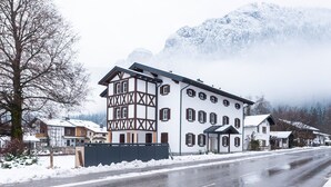 A two-story building with a traditional Alpine architectural style, featuring a prominent corner section with exposed wooden beams. - Hochkalter Vacation Rental (Schönau am Königssee)