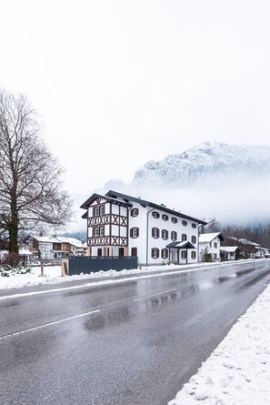 Ein zweistöckiges Gebäude im traditionellen alpinen Baustil, mit einem markanten Eckteil und freiliegenden Holzbalken.