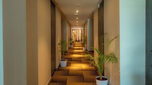 A hallway with a checkered floor pattern, potted plants, and a view into a room with a curtain at the end. - Artis Connect Mysore  (Mysore)