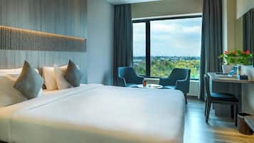Habitación de hotel con una cama grande, un escritorio con una computadora portátil, dos sillas y vista a la ciudad.