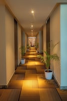 A hotel corridor with a patterned floor, potted plants, and a long view towards the end of the corridor.