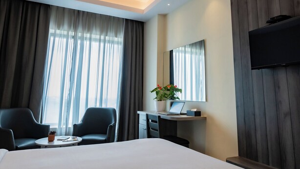 A hotel room with a bed, two chairs, a desk with a laptop, a potted plant, and a TV mounted on the wall. - Artis Connect Mysore  (Mysore)