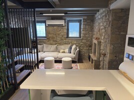 Un espacio de sala cómodo con pared de piedra, un sofá, otomanas y un televisor.