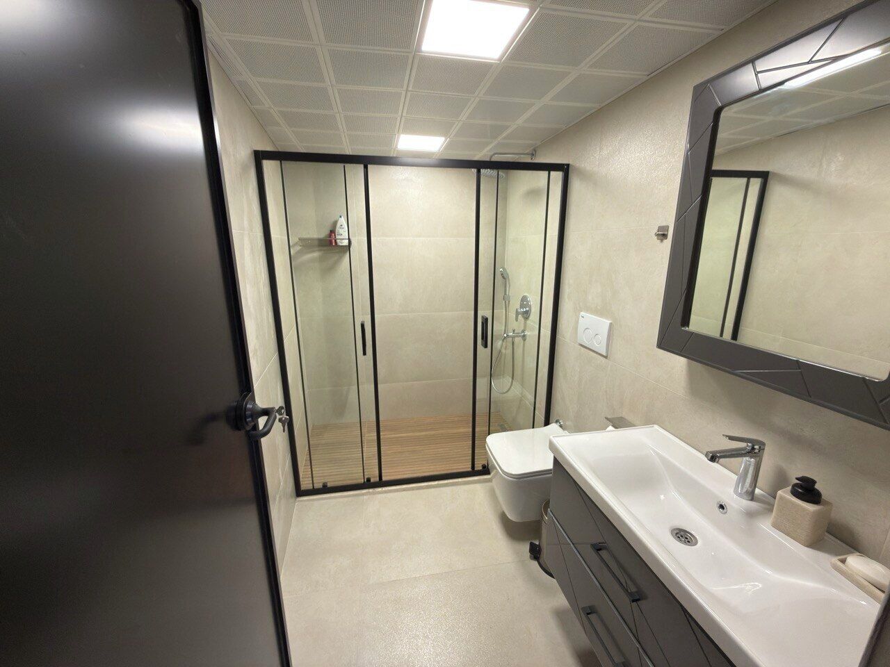 Ein modernes Badezimmer mit Duschkabine aus Glas, einem weißen Waschbecken mit Spiegel und einer Toilette.