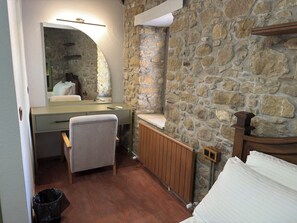 A compact room with a stone wall, a wooden bed, a desk with a chair, and a radiator. - Center Stone Guest House (Gokceada)