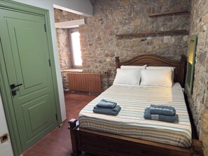 Un dormitorio con pared de piedra, una cama de madera con colcha a rayas y una puerta verde.