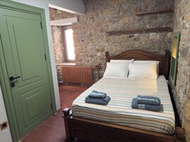 Un dormitorio con pared de piedra, una cama de madera con colcha a rayas y una puerta verde.