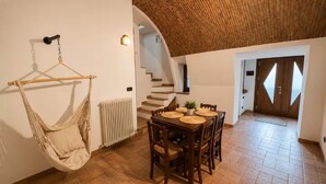 Un espace repas avec une table et des chaises en bois, un fauteuil suspendu et un escalier menant à une autre pièce.