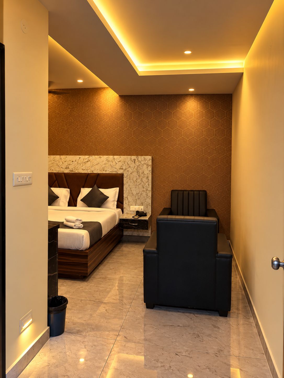 A modern hotel room with a large bed, a seating area, and a marble floor.
