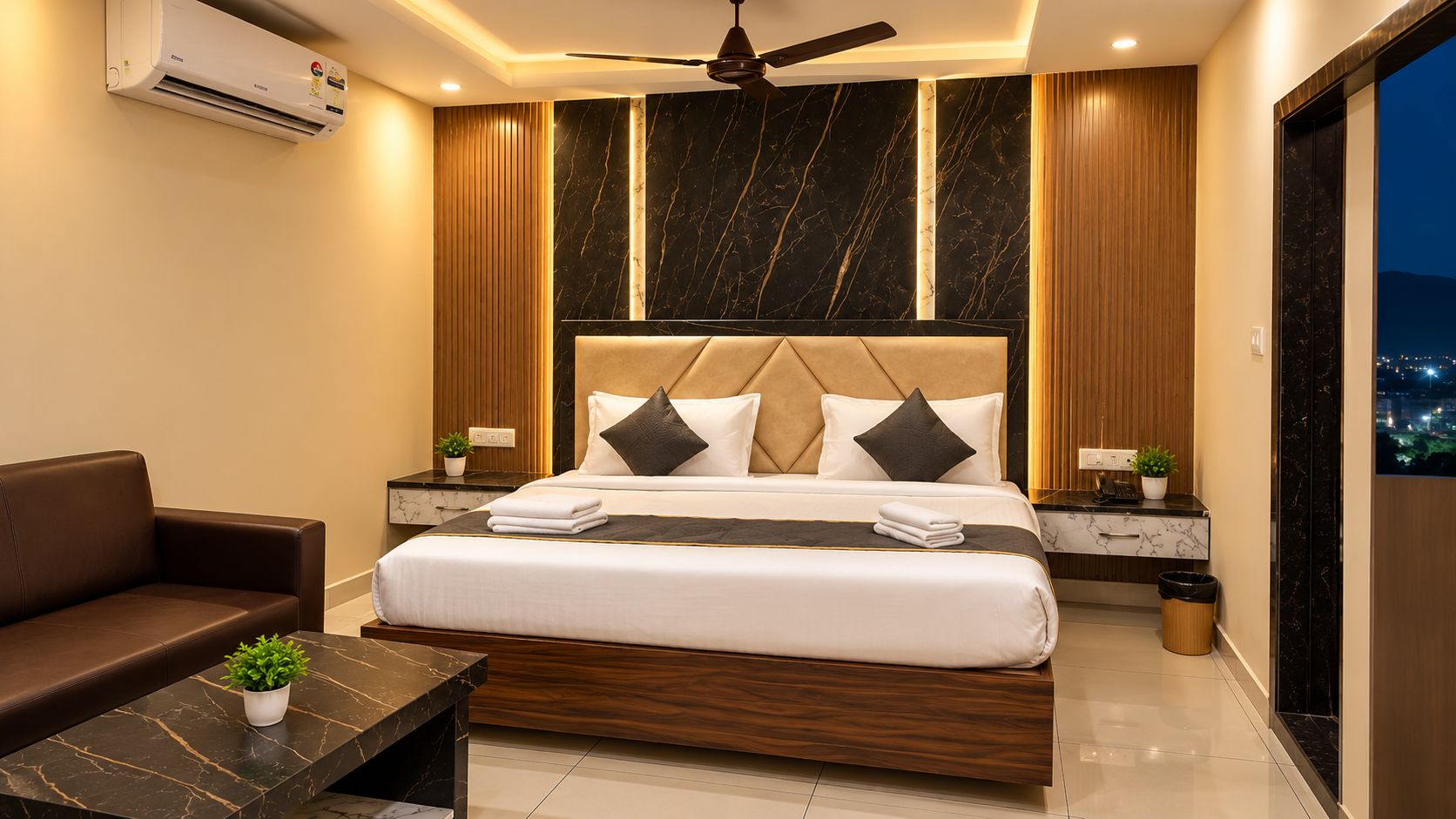 A modern hotel room with a large bed, a sofa, a small table, and a ceiling fan.