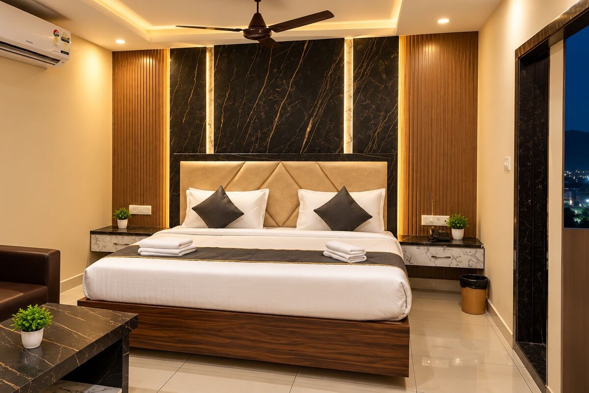 A modern hotel room with a large bed, a sofa, a small table, and a ceiling fan.