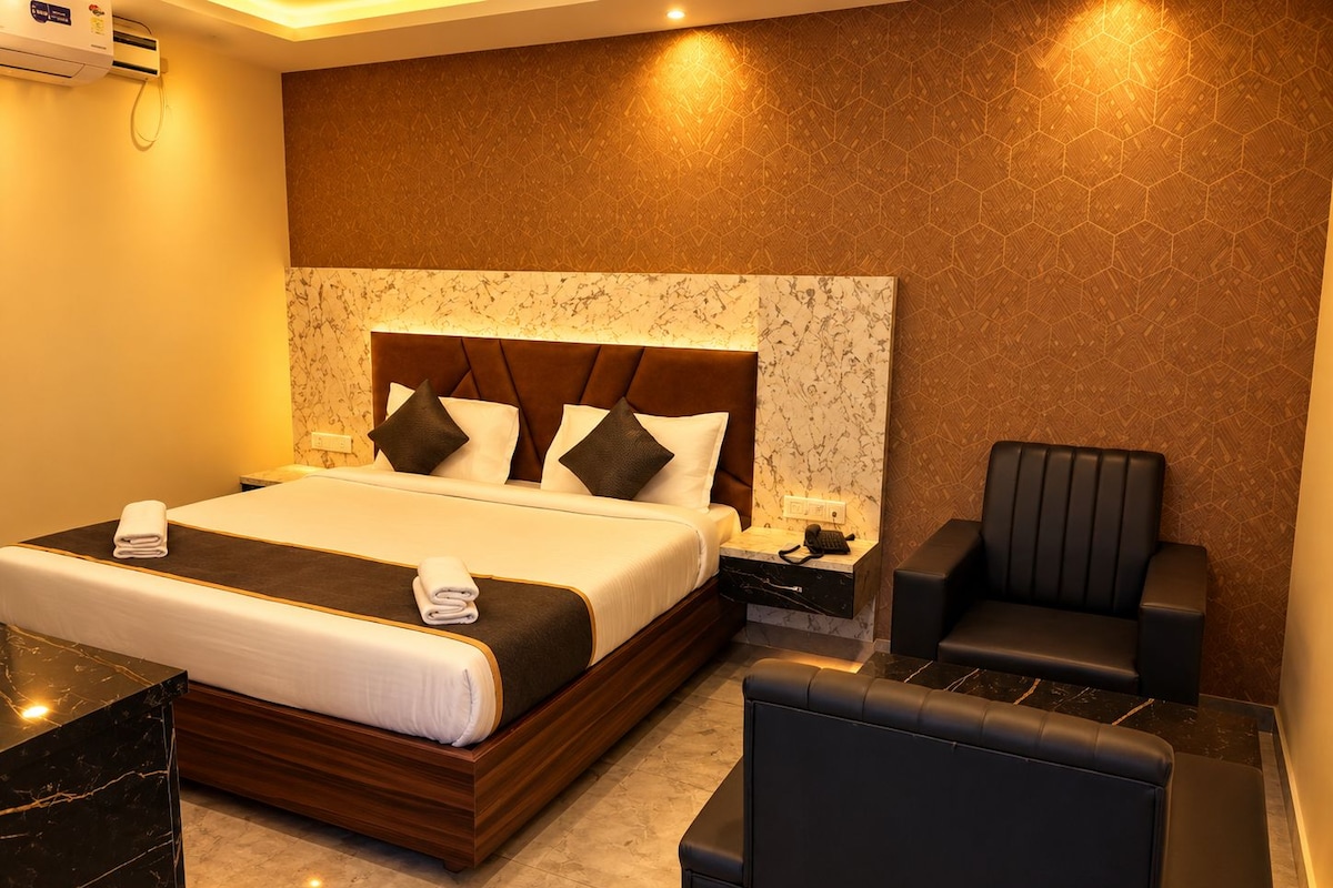 A hotel room with a large bed, a bedside table with a phone, a chair, and a marble floor.