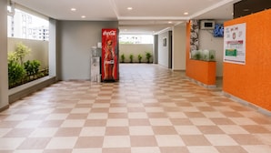 Pasillo de hotel con una máquina expendedora de Coca-Cola, plantas en macetas y una recepción con pared naranja.