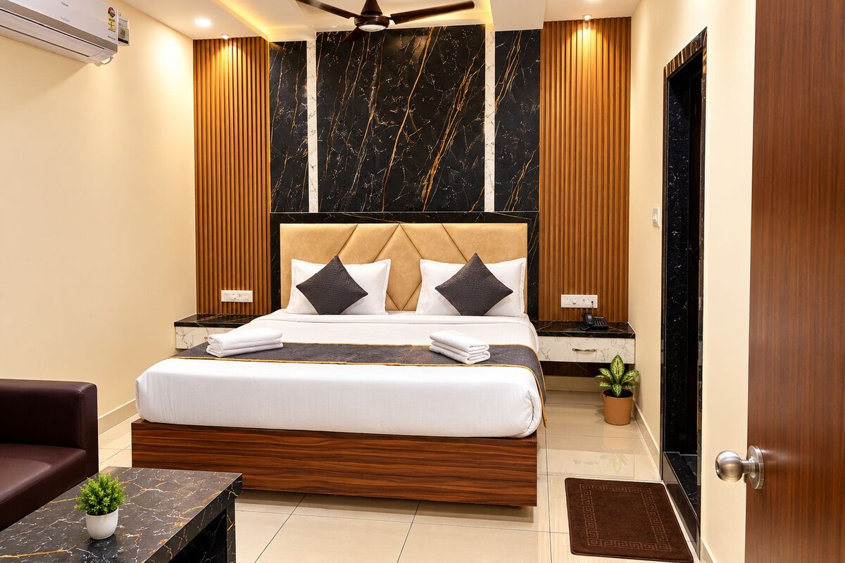 A modern hotel room with a large bed, wooden headboard, marble wall panels, a ceiling fan, and a small potted plant.