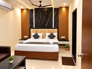 Habitación de hotel moderna con una cama grande, cabecera de madera, paneles de pared de mármol, ventilador de techo y una pequeña planta en maceta.
