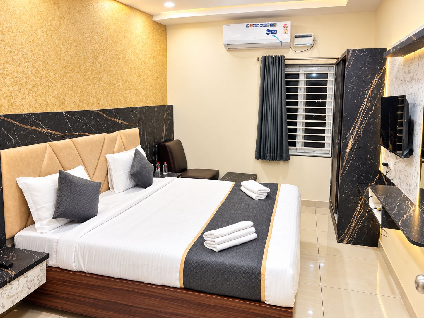 A hotel room with a bed, a desk, a chair, an air conditioning unit, and a television.
