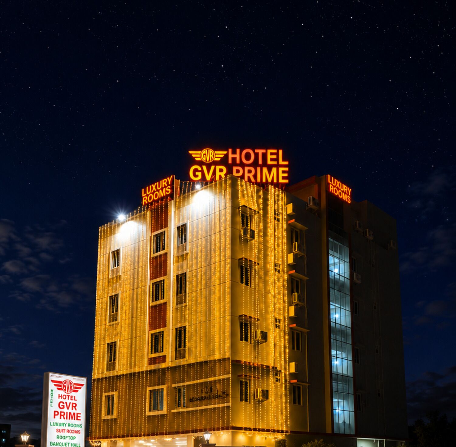 A hotel building with illuminated signage indicating 'HOTEL GVR PRIME' and 'LUXURY ROOMS' at night.