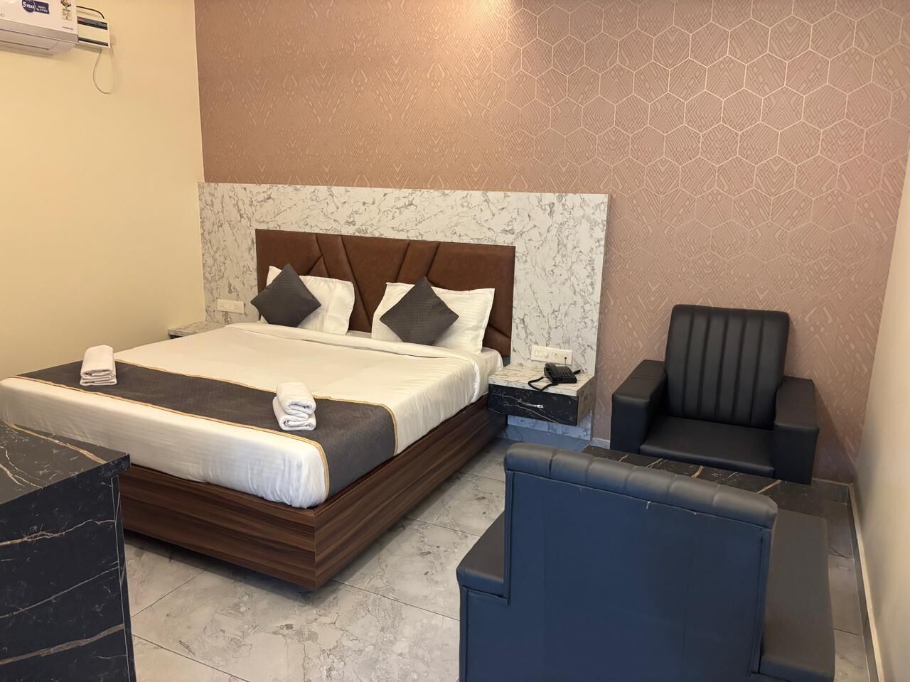 A hotel room with a bed, bedside table, chair, and a marble-patterned wall.