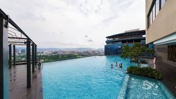 An infinity pool with a city view, surrounded by modern buildings and a wooden deck.