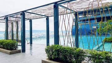 A rooftop pool area with a view of a cityscape, metal railings, and greenery.