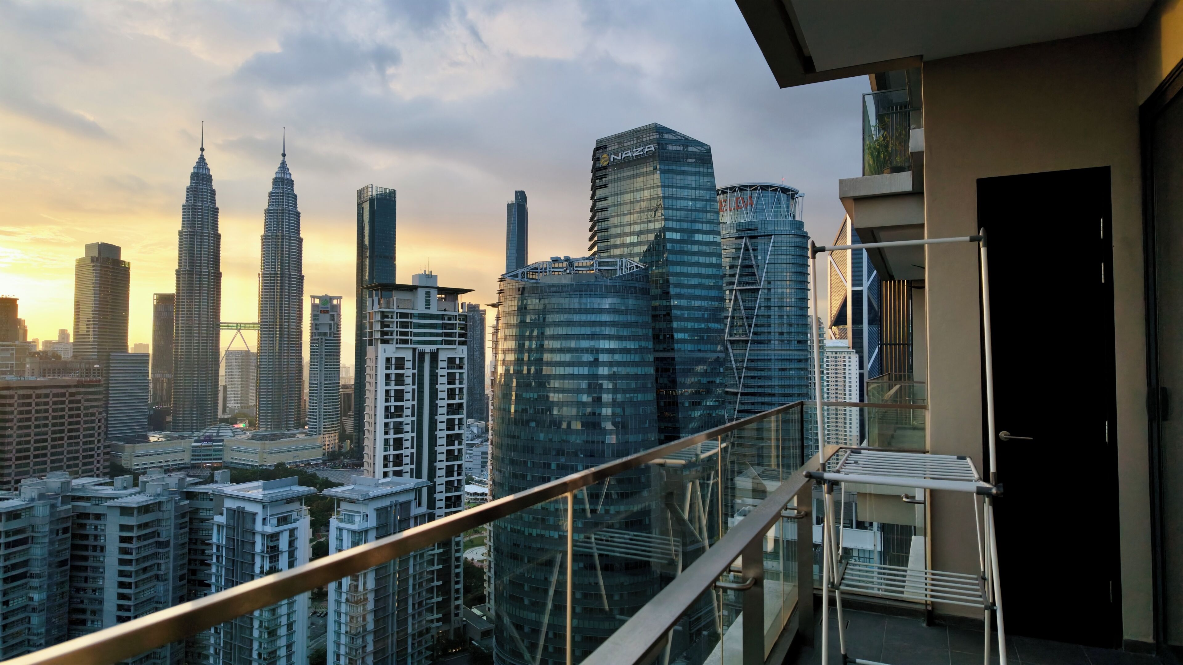 A high-rise building with a glass facade, a balcony with a metal railing, and a clear view of the city skyline.