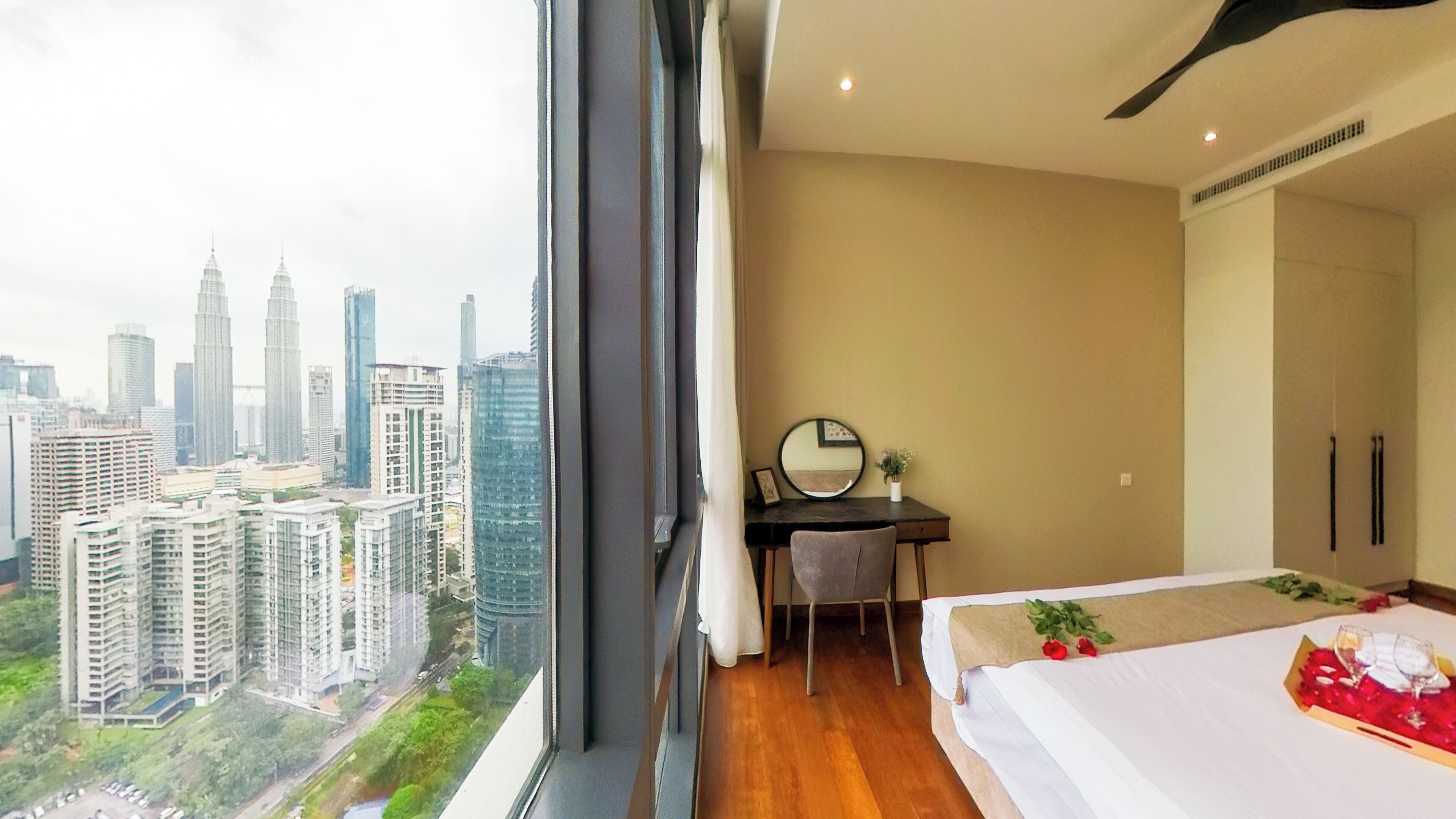 A hotel room with a large window, a bed with a white bedspread, a desk with a chair, and a mirror.