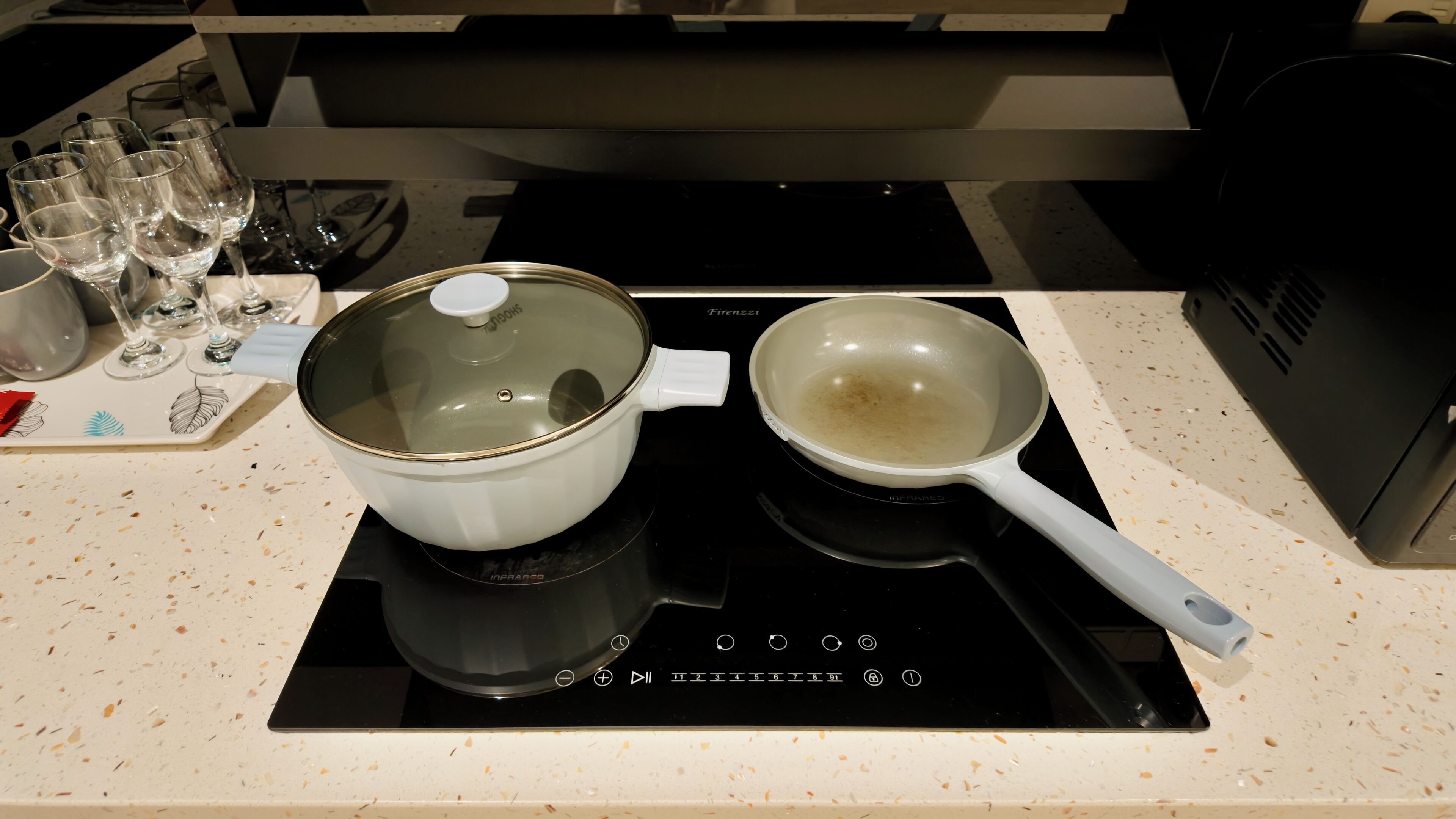 A kitchen with a white pot on an induction cooktop, a frying pan, and several wine glasses on a countertop.