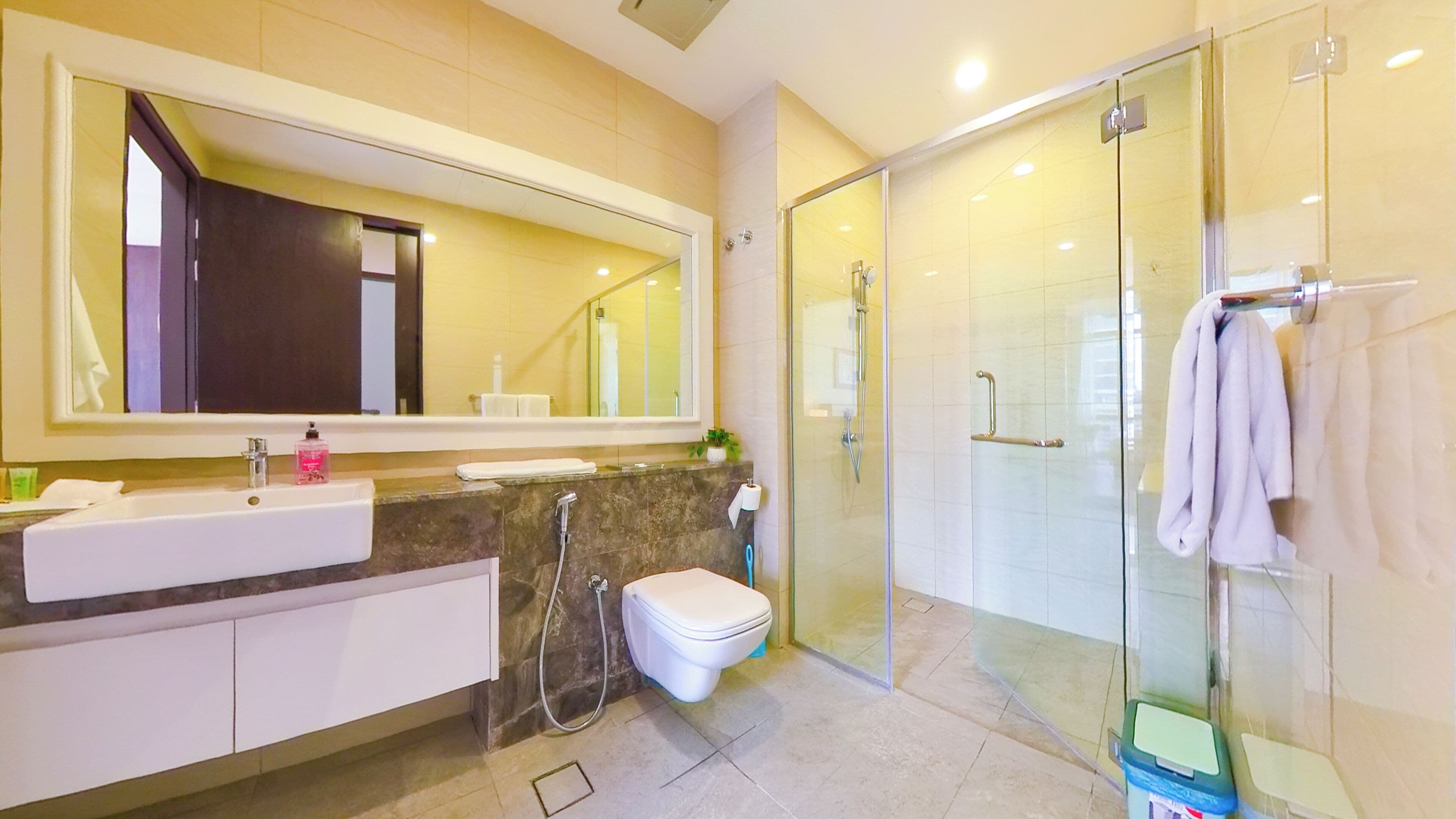 A modern bathroom with a large mirror, a sink, a toilet, and a glass-enclosed shower area.