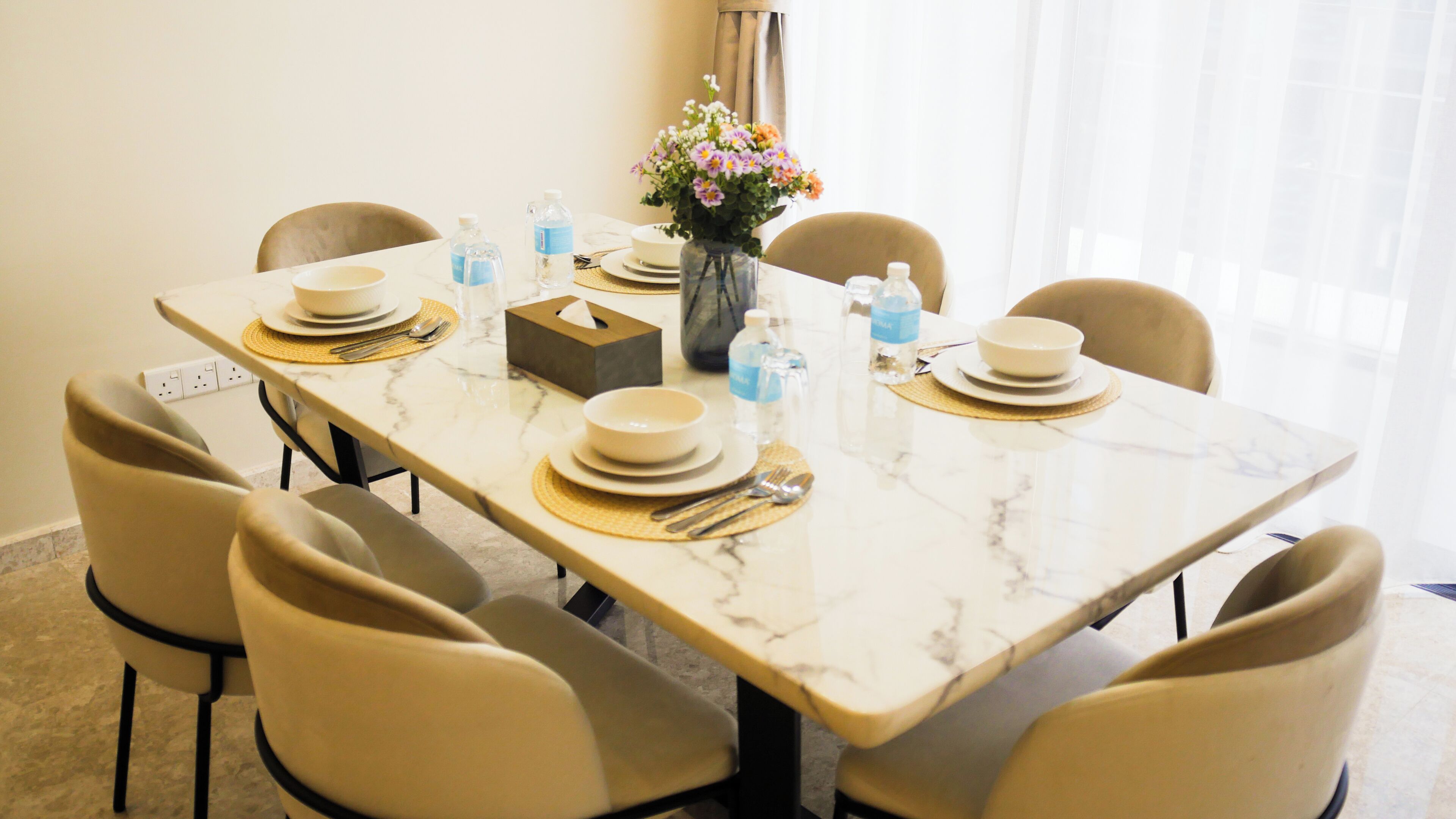 A dining table set with plates, cutlery, and water bottles, surrounded by chairs.