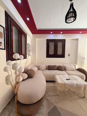 A modern living room with a sectional sofa, a white fluffy ottoman, and a decorative vase with white flowers.