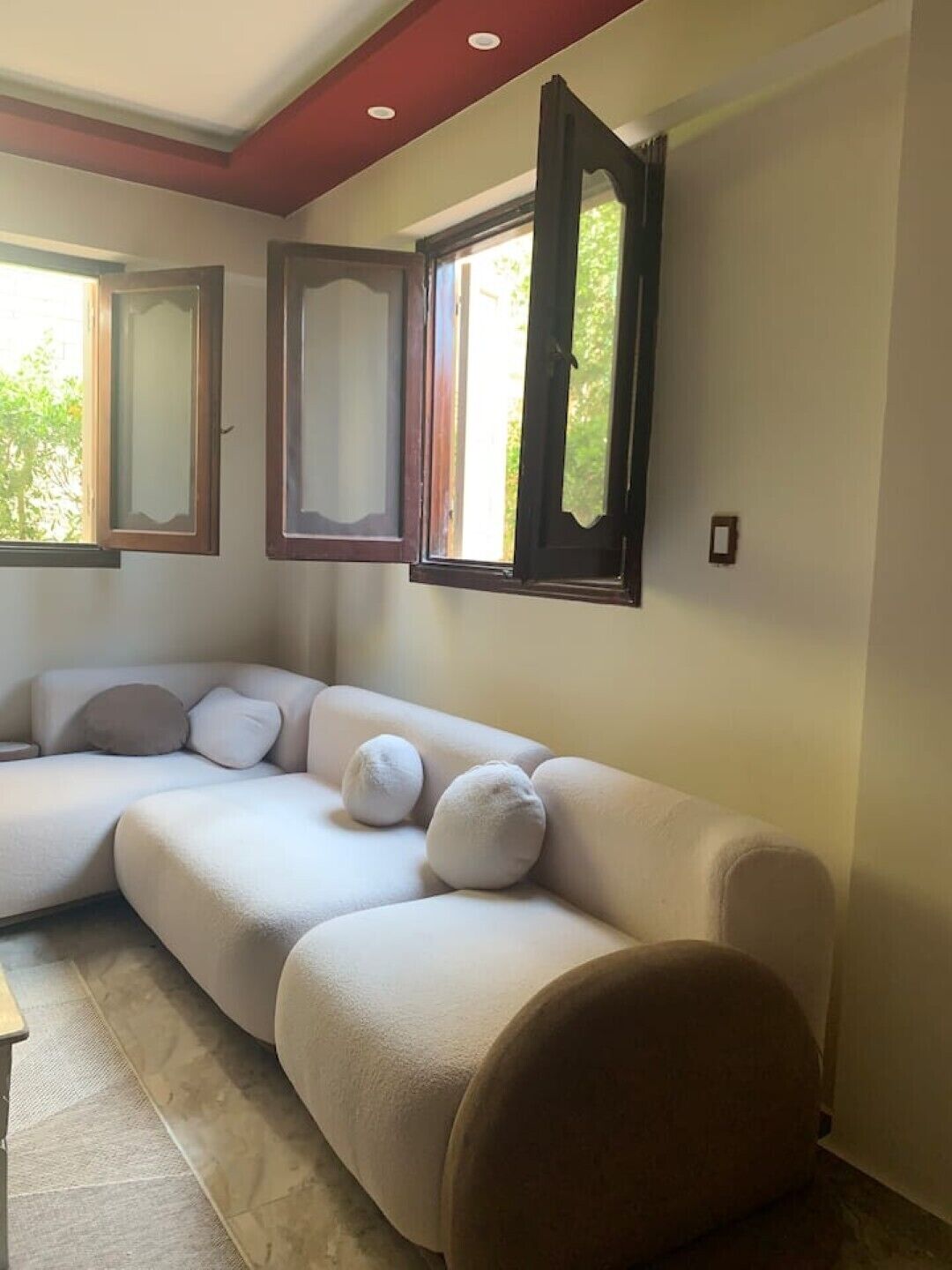 A modern living room with a sectional sofa, a round chair, and three windows with open shutters.