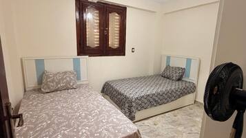 A bedroom with two beds, a ceiling fan, and a window with wooden shutters.