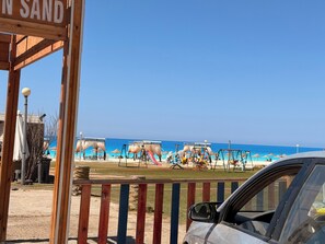 A beach with a wooden structure labeled 'IN SAND,' a playground with swings and slides, and a clear blue sky. - Chalet in Horus Village and Golden Sands, North Coast (North Coast)