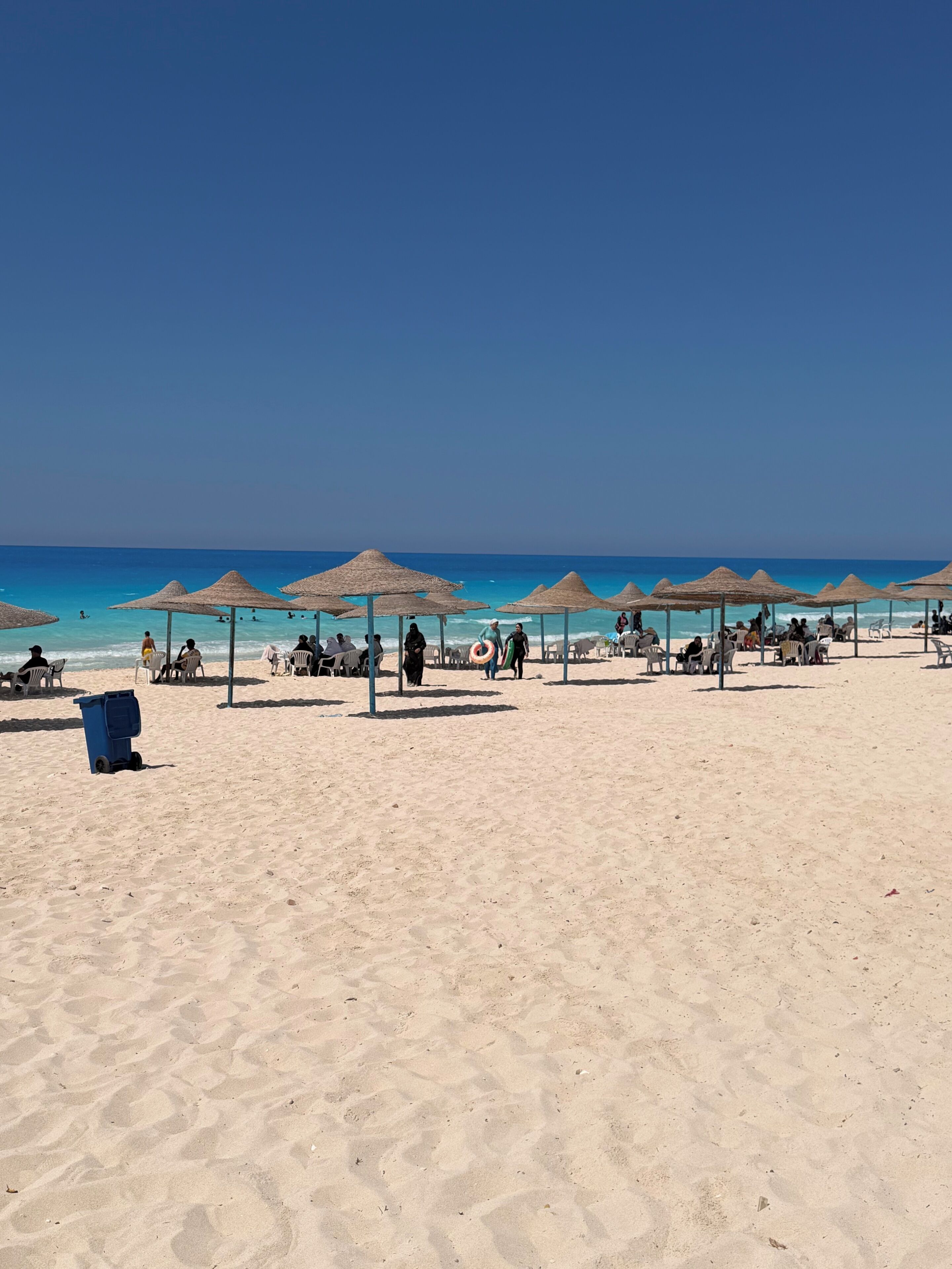 Une plage avec des parasols en chaume et des chaises longues, un ciel bleu azur et l’océan en toile de fond.