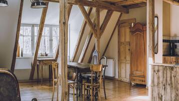 A rustic room with exposed wooden beams, a wooden dining table with chairs, a wooden cabinet, and a window with a view.