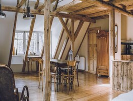 Um quarto rústico com vigas de madeira aparente, uma mesa de jantar de madeira com cadeiras, um armário de madeira e uma janela com vista.