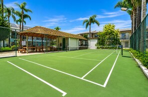 A tennis court with a wooden pavilion, surrounded by a fence and palm trees. - Sea Breeze 2-bedroom apartment with AC in Mandurah (Mandurah)