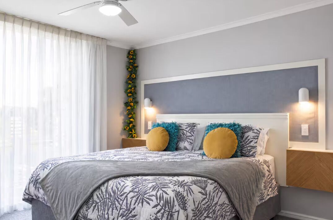 Une chambre à coucher comprenant un lit, un ventilateur de plafond, une lampe fixée au mur et une plante décorative.