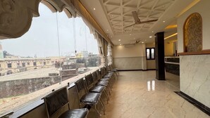 A hotel lobby with a long row of chairs, a reception desk, and a view of the cityscape through large windows. - Ramanjaneya Eecutive Hotel Udupi (Samudrapur)
