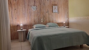 Quarto com cabeceira de madeira, cama com colcha acolchoada, duas luminárias de cabeceira e um interruptor de luz fixado na parede.