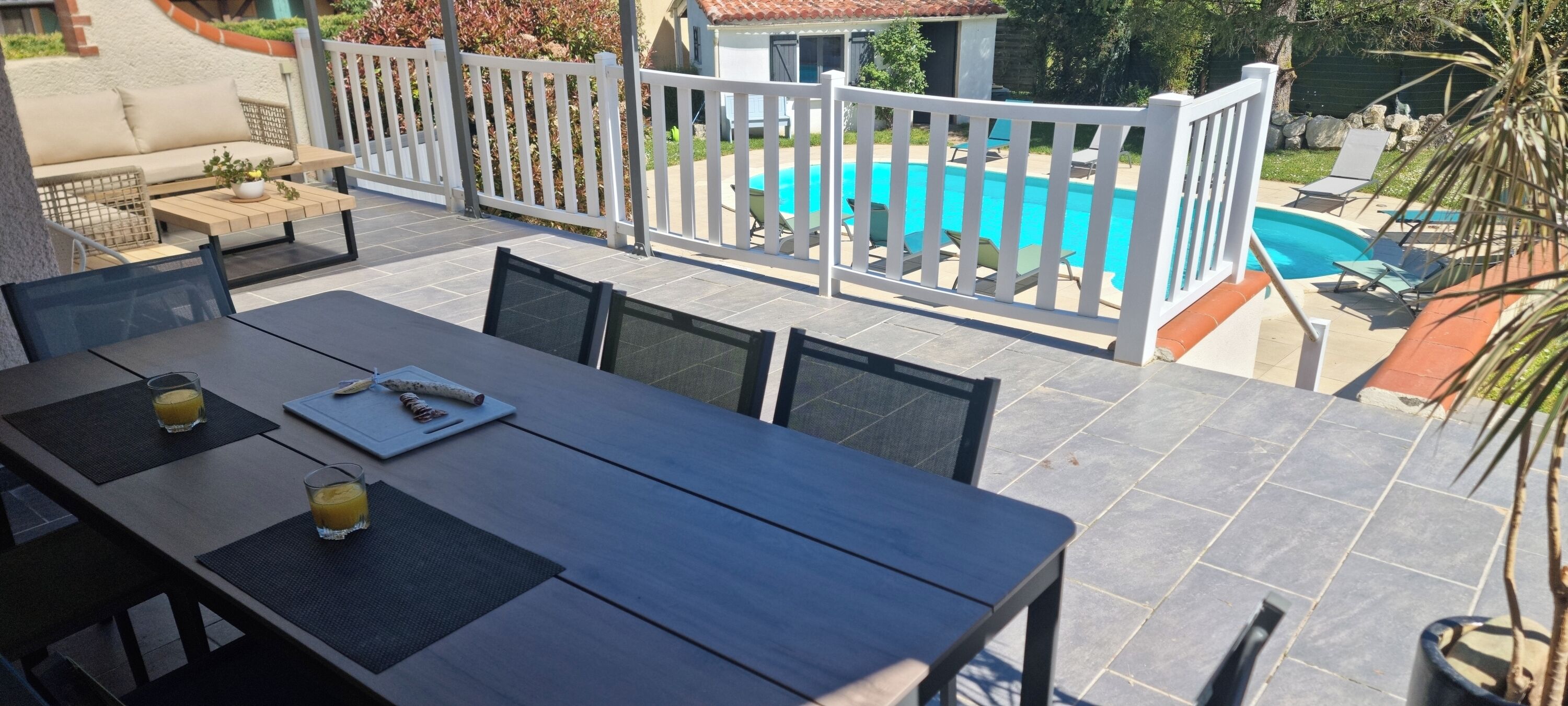 A patio with a pool, outdoor seating, and a table with drinks.