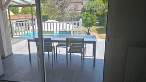 Um pátio com mesa e cadeiras, cerca branca e vista para uma piscina e vegetação.