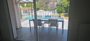 Eine Terrasse mit Tisch und Stühlen, ein weißer Zaun sowie Blick auf einen Pool und Grünflächen.