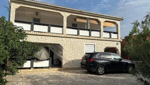 A two-story building with a balcony, a covered entrance, and a parked car. - Relax and be well in this fresh apartment for 4 + Parking on the island of Vir (Vir)
