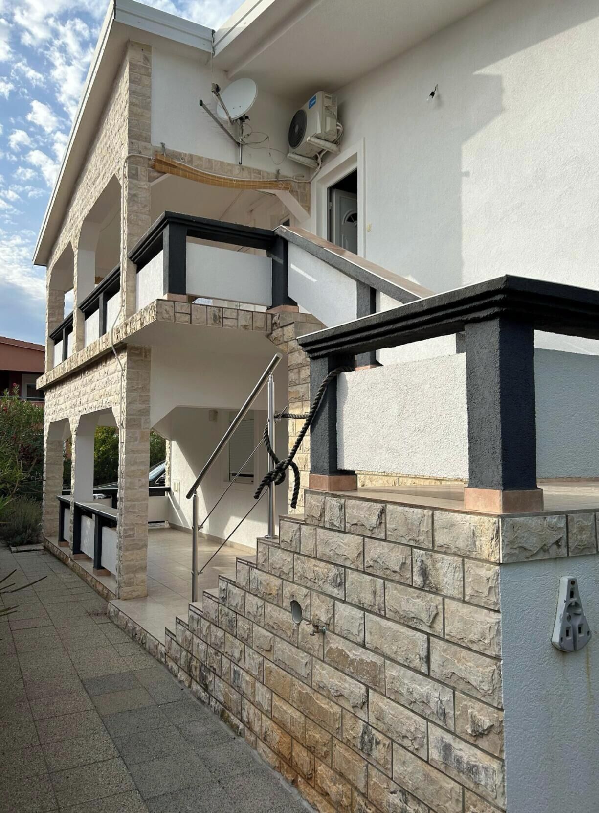 A multi-story building with a stone facade, a balcony, and a staircase leading to the entrance.