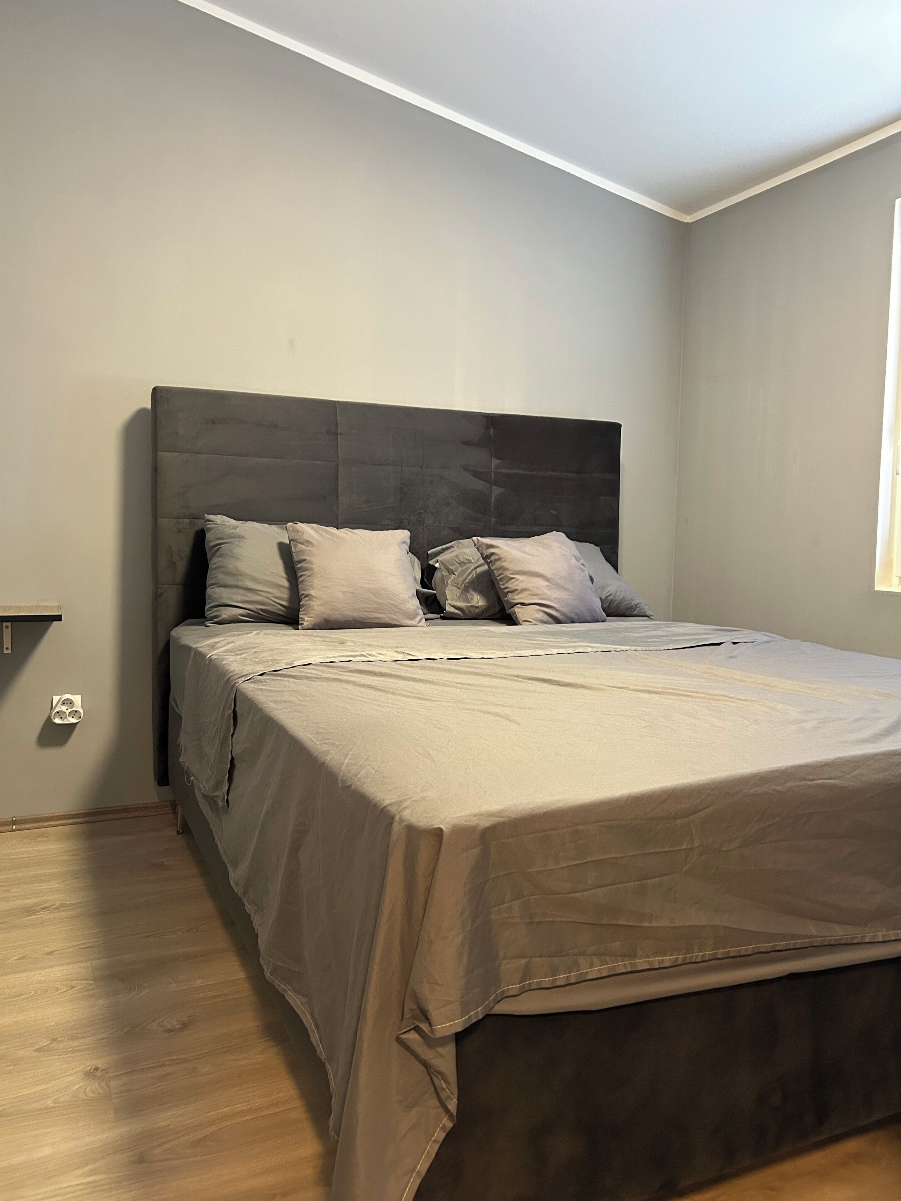 Un dormitorio con una cama grande, cabecera y una ventana.