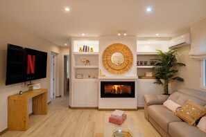 A modern living room with a flat-screen TV, a fireplace, and a sofa.