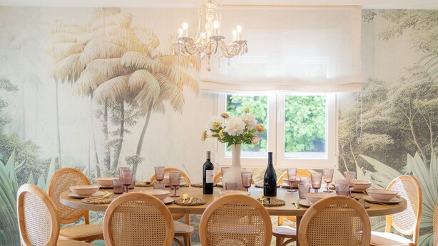 A dining area with a round table set for six, surrounded by wicker chairs, a chandelier, and a large floral mural on the wall. - LUXURY VILLA PARAISO ALICANTE—Heated saltwater pool, fireplace, gym, Netflix (Monforte del Cid)