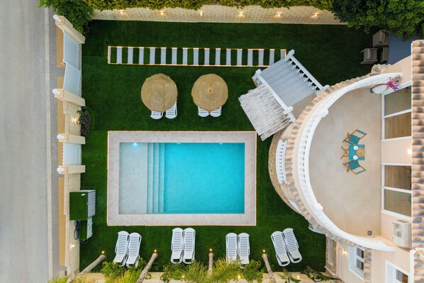 A rooftop pool area with a rectangular pool, lounge chairs, and a small seating area with umbrellas.